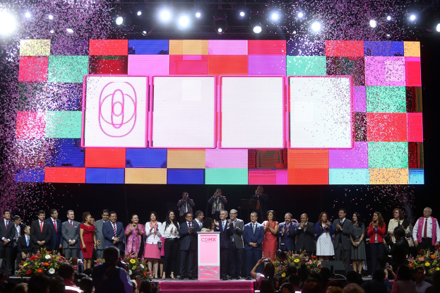 Gruppe von Menschen auf einer Bühne mit einem Podium, Blumensträußen, Kameras und einem großen Bildschirm, der Lichter für die Eröffnungszeremonie des 2018 China International Film Festivals anzeigt.