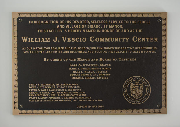 Schwarzes rechteckiges Schild mit weißer zentrierter Beschriftung, die "William J. Vesco Community Center" lautet, angebracht an einer Gebäudewand.