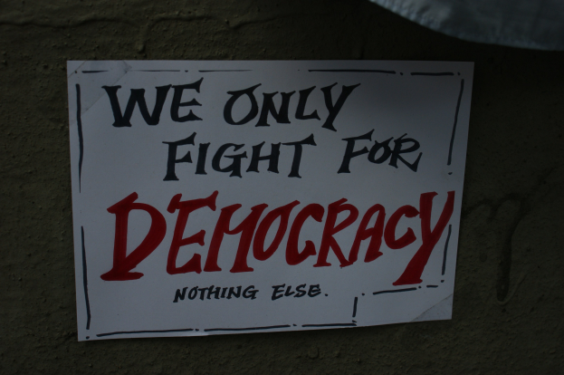 Weißer Bericht mit den Worten "Wir kämpfen nur für Demokratie" an einer Wand befestigt.