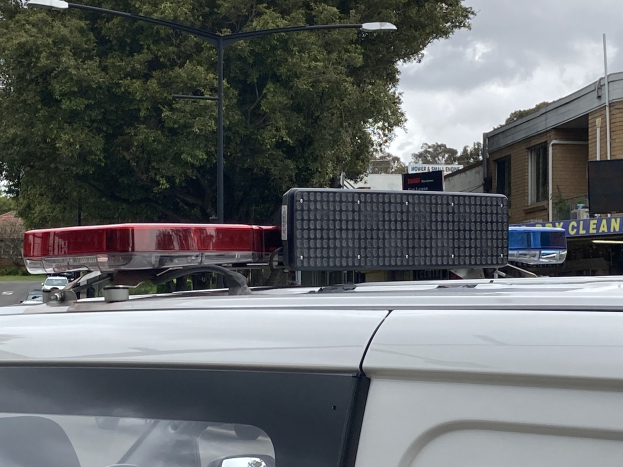 Polizeiauto mit blinkenden Lichtern auf einer Straße neben einer Schule geparkt, umgeben von Gebäuden, Bäumen und Strommasten.