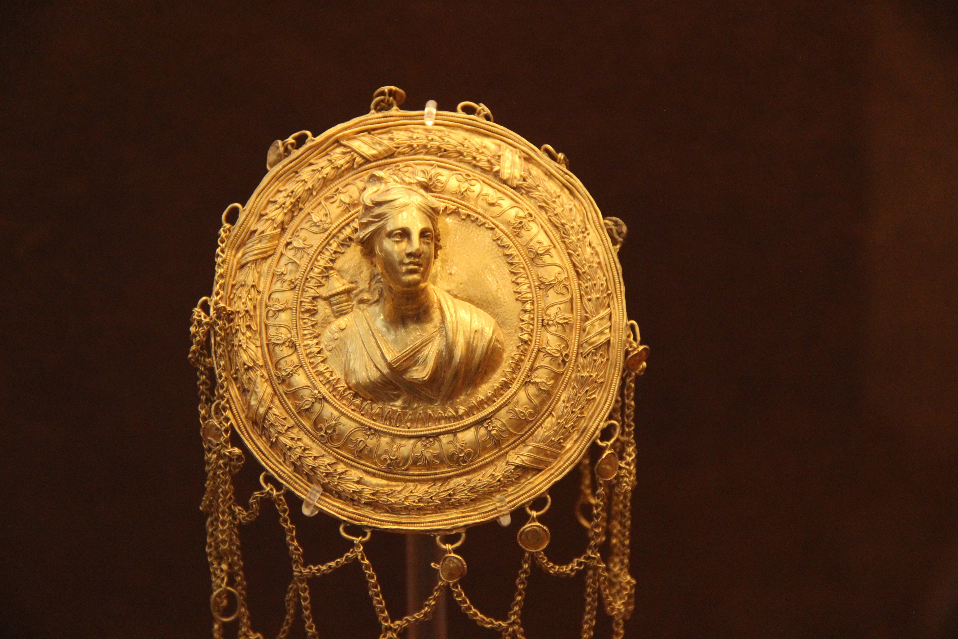 Goldene Medaille mit einem Frauengesicht auf dunklem Hintergrund, mit aufwändigen Details verziert.
