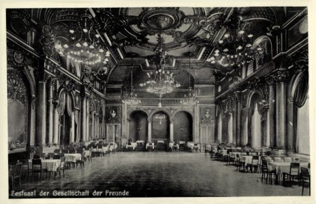 Schwarzes und weißes Foto eines großen Raums mit Tischen, Stühlen, Säulen, Bögen und Deckenleuchter, beschriftet mit 'Festival der Gesellschaft der Freunde, Berlin' unten.