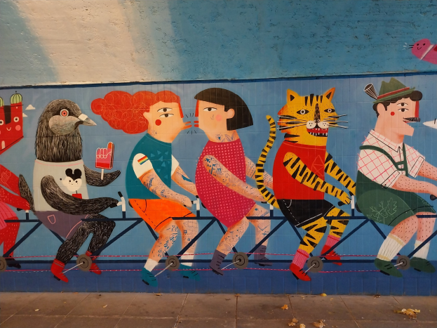 Ein Wandgemälde auf einem Gebäude in London, das eine Gruppe von Menschen auf Fahrrädern zeigt, mit einer Straße und einem Himmel im Hintergrund.