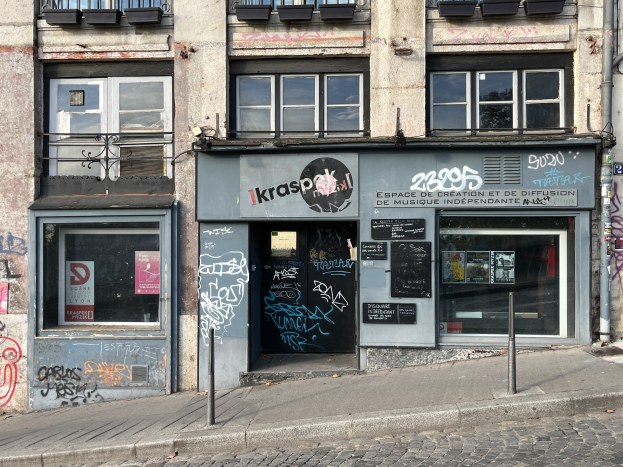 Ein mehrstöckiges Gebäude mit Fenstern, Geländern, Türen, Texttafeln, Plakaten, Pfählen und Graffiti an der Seite, das sich über einer Straße befindet.