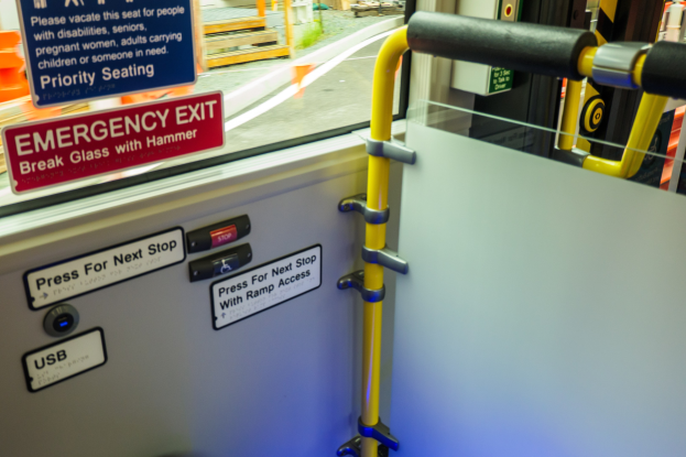 Notausgangsschild an der Seite eines Zuges, mit Tür, Griff und Glasfenster, das Straße, Pfähle und andere Außenobjekte zeigt.