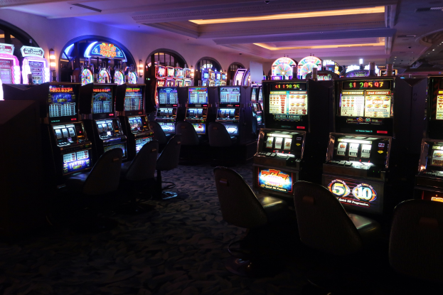 Reihe von Spielautomaten zum Verkauf in einem Casino mit Stühlen und Deckenleuchten sichtbar.