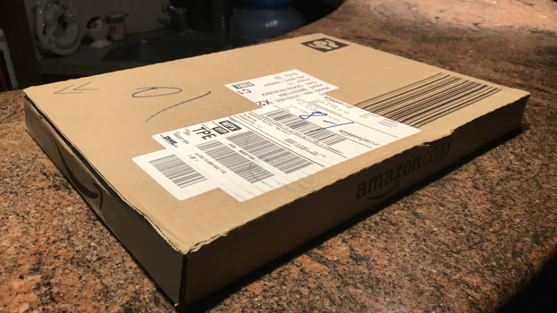 Kartonbox beschriftet mit 'Amazon Prime Day' auf einem Tresen stehend mit Gegenständen im Hintergrund.