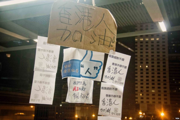 Gruppe von Menschen protestiert nachts vor einem Gebäude mit beleuchteten Schildern gegen ein Social-Media-Verbot.