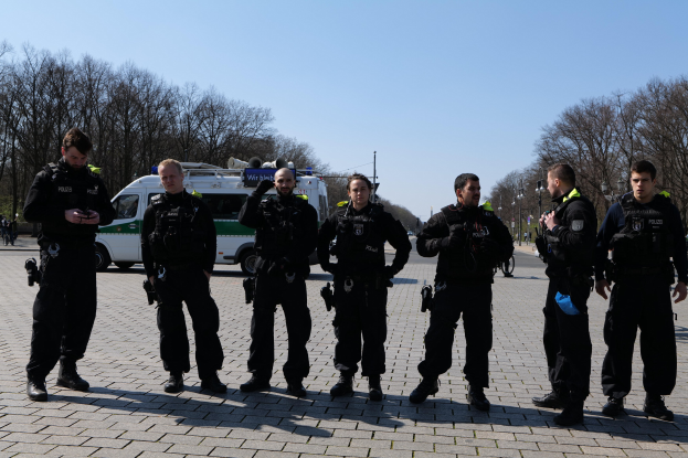Eine Gruppe von Polizisten vor einem Rettungswagen auf einer Straße mit Bäumen, Laternen und einem klaren Himmel.