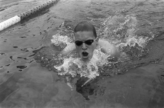 Schwarzes und weißes Foto eines Schwimmers in der Mitte eines Rennens, der eine Schwimmbrille trägt und um ihn herum sind Bahnmarkierungen sichtbar.