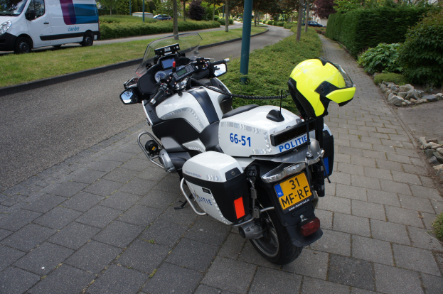 Polizeimotorrad am Straßenrand mit Helm auf dem Sitz, umgeben von Bäumen, Strommasten, Gebäuden, Grünflächen und anderen Fahrzeugen.
