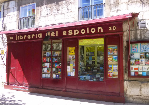 Eine Buchhandlung mit rotem Markisen namens "Libreria del Espolon" mit ordentlich sortierten Büchern in Regalen, untergebracht in einem Gebäude mit Fenstern und Geländern.