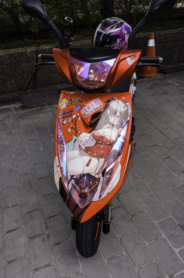 Oranger Roller auf der Straße geparkt mit Helm darauf, Verkehrskegel, Wand und Bäume im Hintergrund.