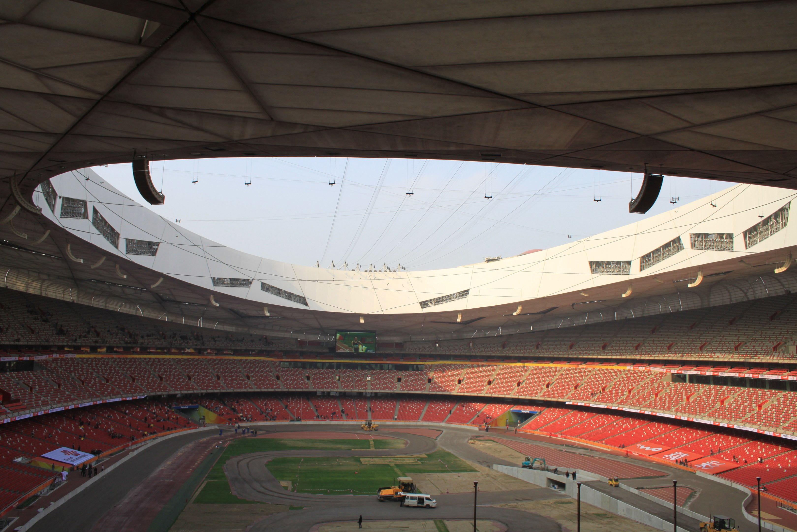 Olympiastadion in Rio de Janeiro mit Zuschauern auf Tribünen, Bodenfahrzeugen, Strommasten, einem Schuppen und sichtbarem Himmel.