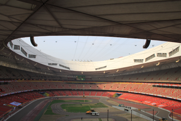 Olympiastadion in Rio de Janeiro mit Zuschauern auf Tribünen, Bodenfahrzeugen, Strommasten, einem Schuppen und sichtbarem Himmel.