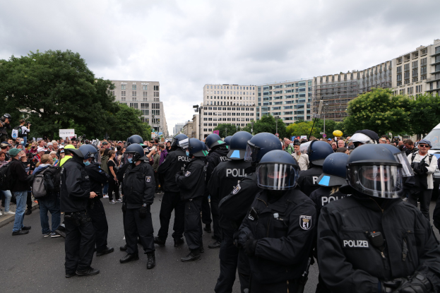 Eine große Gruppe von Polizisten steht vor einer Menge während einer Demonstration auf einer Straße in Berlin, Deutschland, wobei einige Individuals Kameras halten.