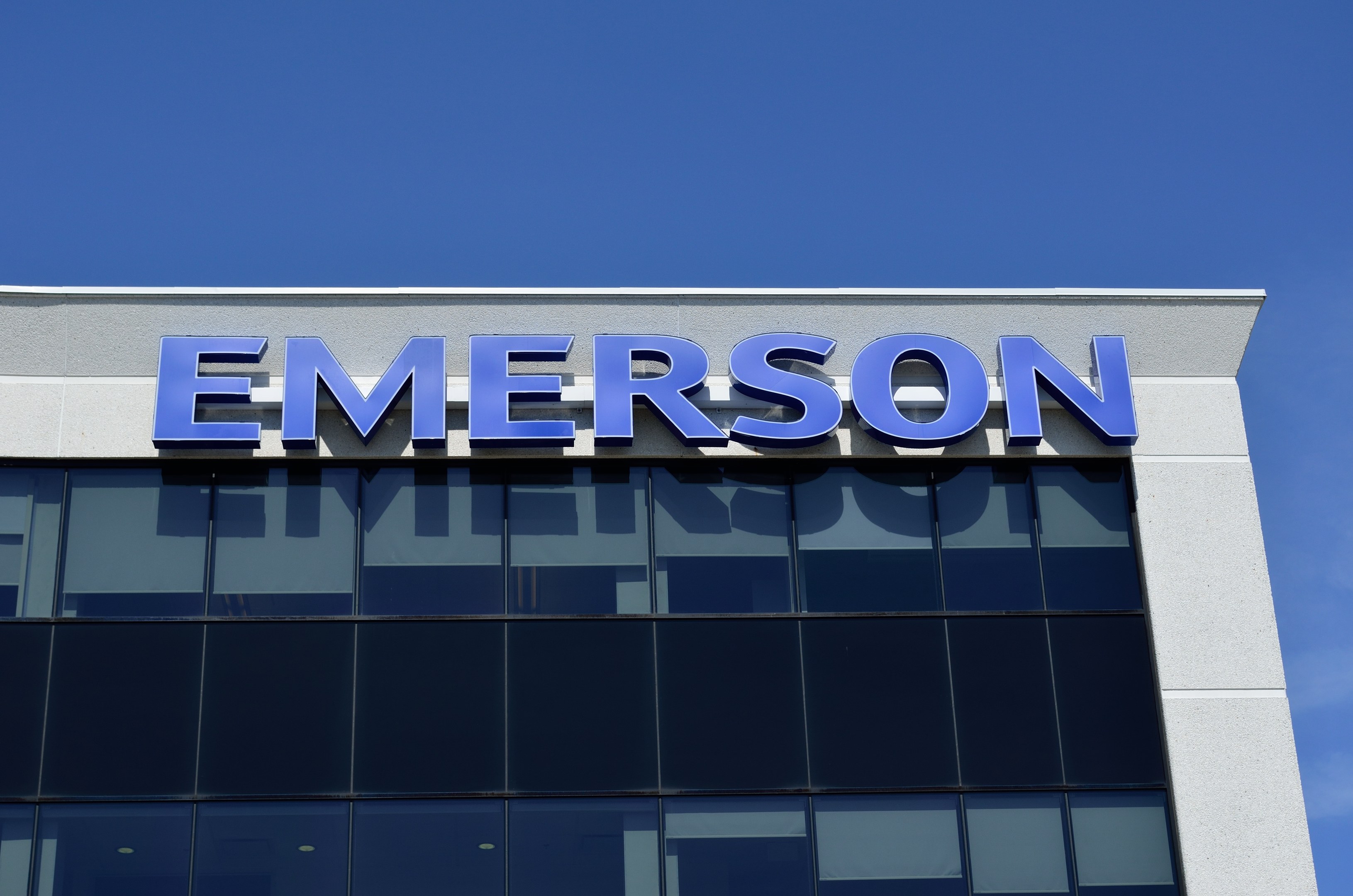 Emerson-Logo auf einem Gebäude mit Text, der besagt "Emerson investiert 1,5 Milliarden US-Dollar in den USA" vor einem klaren blauen Himmel.