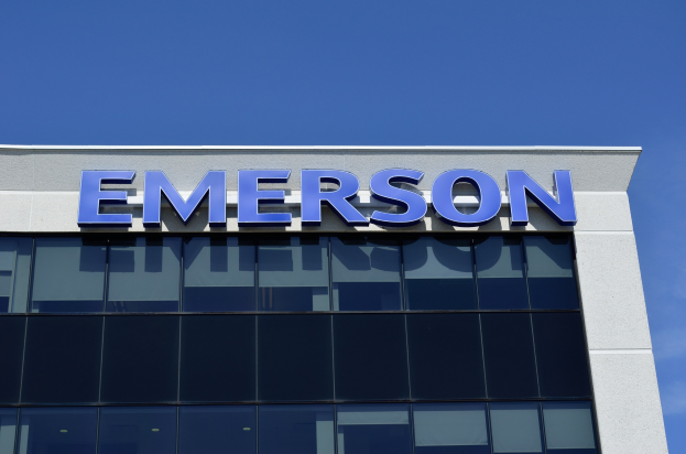 Emerson-Logo auf einem Gebäude mit Text, der besagt "Emerson investiert 1,5 Milliarden US-Dollar in den USA" vor einem klaren blauen Himmel.