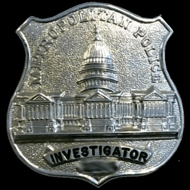 Ein silbernes Polizeiabzeichen mit dem Wort "Ermittler" darauf vor einem weißen Hintergrund.