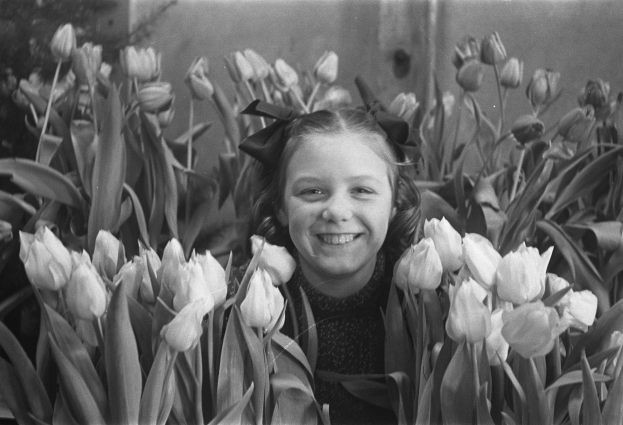 Ein junges Mädchen, das in einem Schwarz-Weiß-Foto umgeben von leuchtenden Tulpen lächelt.