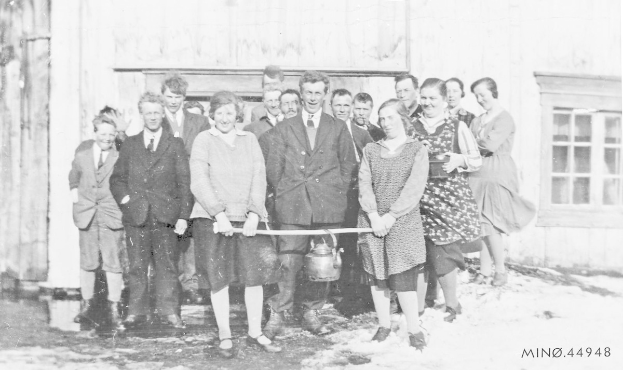 Schwarzes und weißes Foto von Menschen, die ein Band vor einem Gebäude mit einem Fenster und einer Tür halten und bei einer Schul-Eröffnungsfeier lächeln.