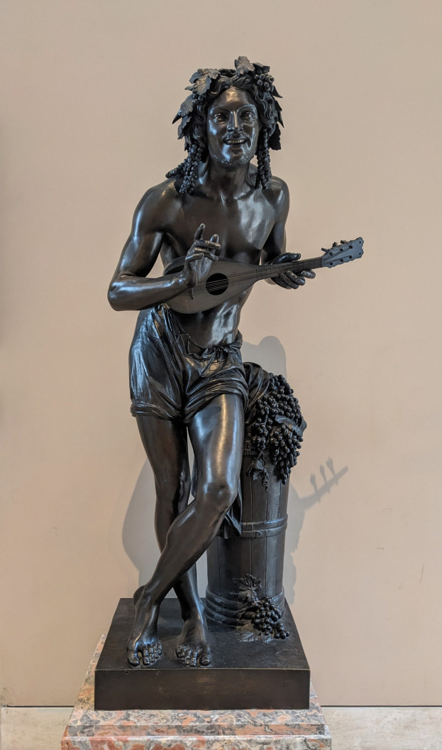 Bronzestatuette eines Mannes, der eine Gitarre spielt, vor einer Wand mit einem Boden darunter.