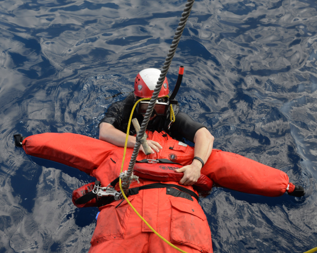 Retter in rotem Lebensjackett und Helm im Wasser mit einem Seil am Rücken.