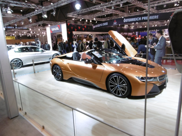 Ein stylischer schwarzer BMW i8 Roadster mit Chromakzenten auf der IAA in Frankfurt umgeben von formell gekleideten Gästen in einer Atmosphäre der Aufregung.