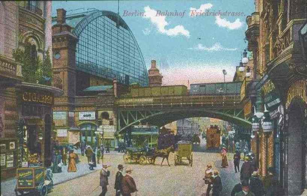 Schwarz-weiß-Postkarte einer belebten Berliner Straße mit Fußgängern, Pferdewagen, Gebäuden, Laternen, einer Brücke und einem bewölkten Himmel mit Text oben.