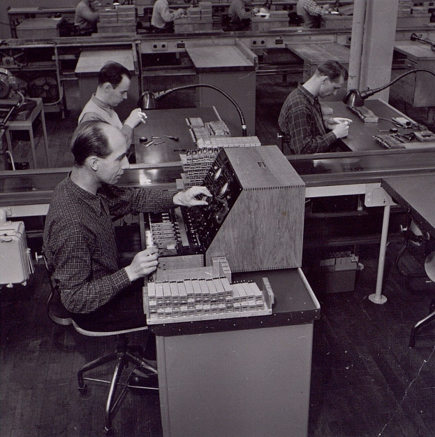 Schwarzes und weißes Bild von Männern, die an Computern in einer Fabrik arbeiten.