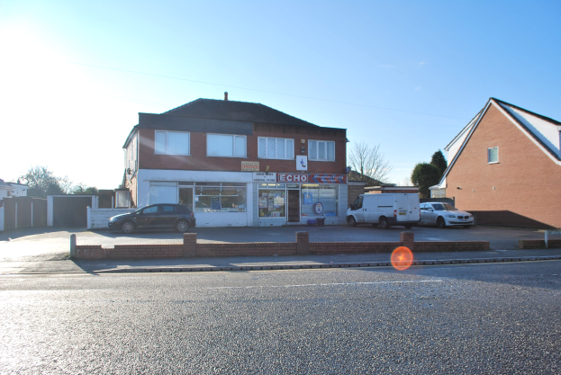 Gewerbeimmobilie zum Verkauf an St Johns Road, Luton, Bedfordshire, mit Gebäuden, Fahrzeugen, einer Wand, Bäumen und einem bewölkten Himmel.
