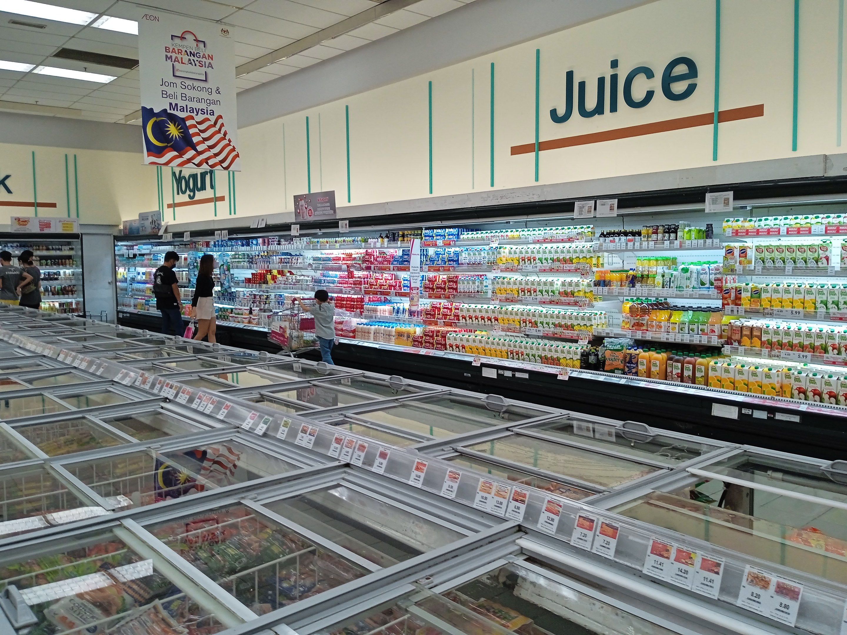 Ein hell erleuchteter Saftladen mit Regalen voller Getränke, frischem Obst und anderen Lebensmitteln, mit einigen Kunden und Deckenlampen.