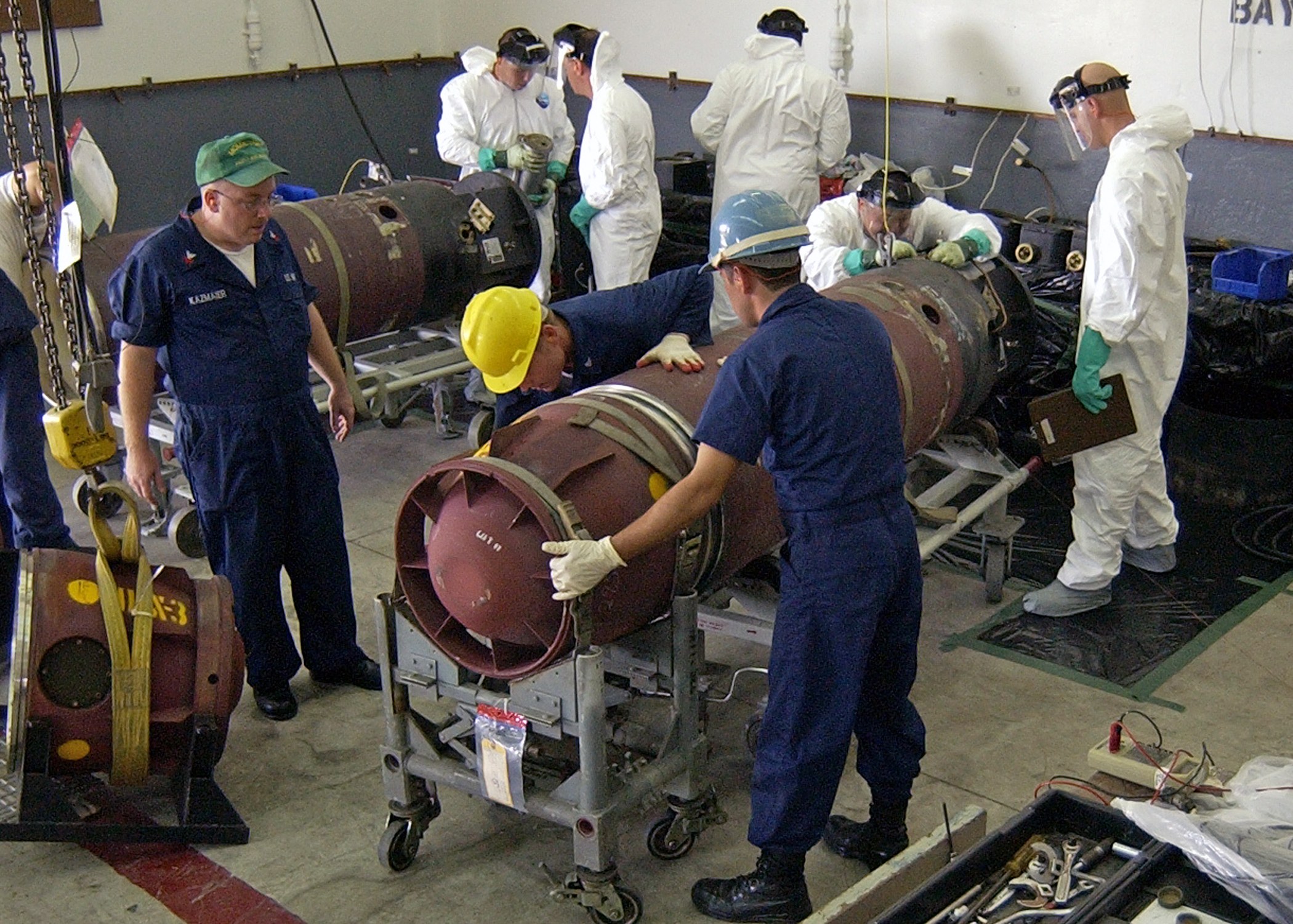 Eine Gruppe von Männern in Helmen und Handschuhen, die eine große Bombe in einer Fabrik entschärfen.