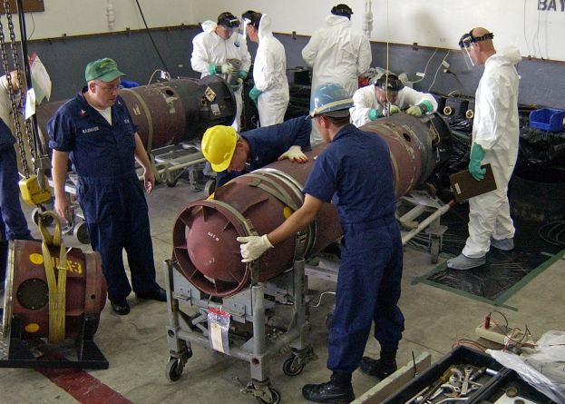 Eine Gruppe von Männern in Helmen und Handschuhen, die eine große Bombe in einer Fabrik entschärfen.