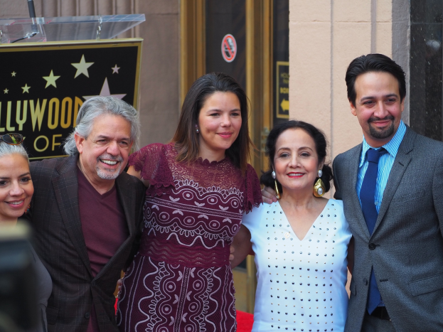 Eine Gruppe von Menschen, die auf einem roten Teppich stehen, lächeln und für ein Foto posieren, mit einer Kamera auf der linken Seite, einer Tafel mit Text, einem Glaspodest und einer Wand im Hintergrund.