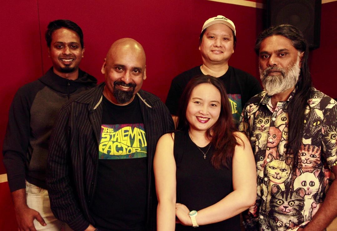 Eine Gruppe von Menschen, die zusammen in einem Aufnahmestudio stehen und vor einer roten Wand posieren.