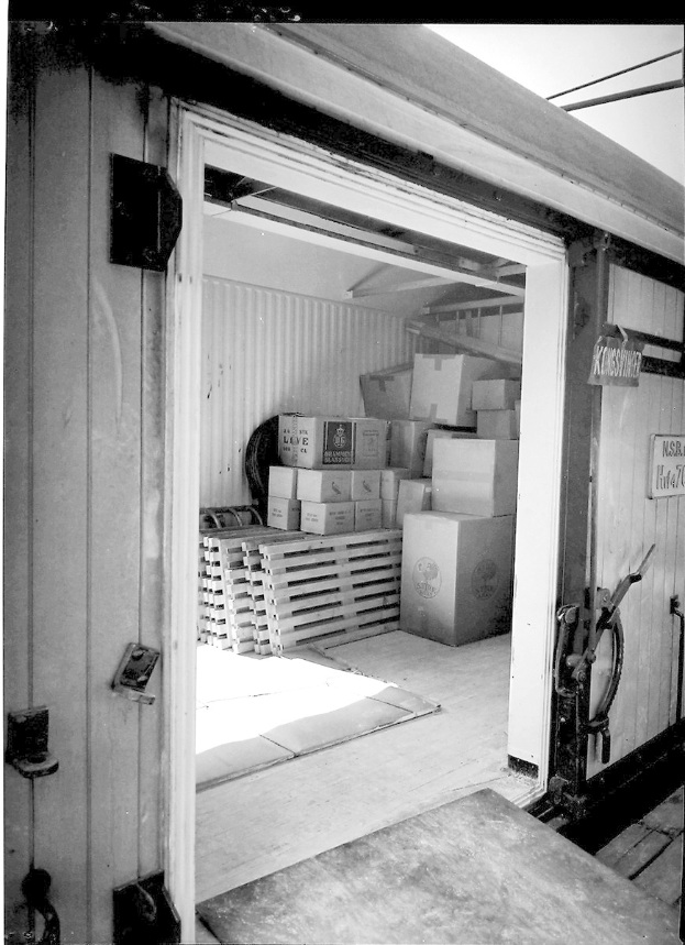 Schwarzes und weißes Foto eines metallenen Seecontainers mit einer Tür auf der linken Seite, gefüllt mit ordentlich gestapelten Kartons.