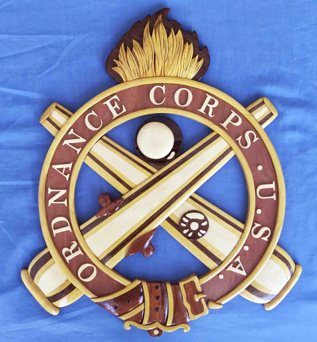 Holztafel mit "Ordnance Corps"-Text, zeigt ein geschnitztes weißes Stern auf einem navyblauen Hintergrund mit goldener Umrandung, auf blauem Tuch montiert.