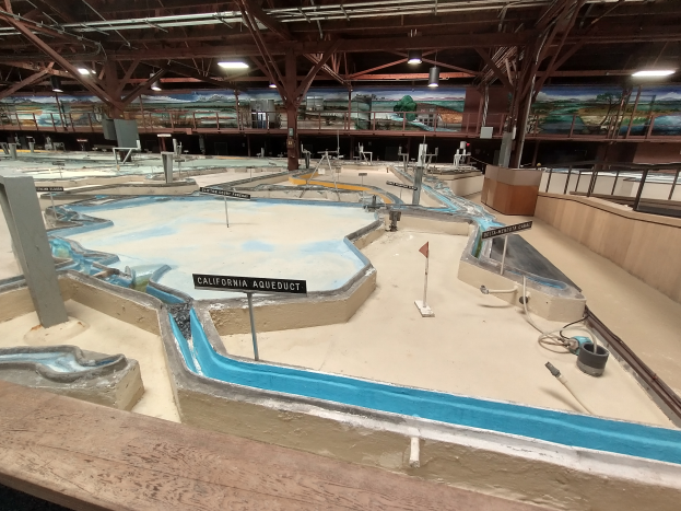 Ein großes Indoor-Wasserpark mit mehreren Wasserrutschen, Pfählen, Texttafeln, Deckenleuchten und Wandgemälden, das wie ein Minigolfplatz gestaltet ist.