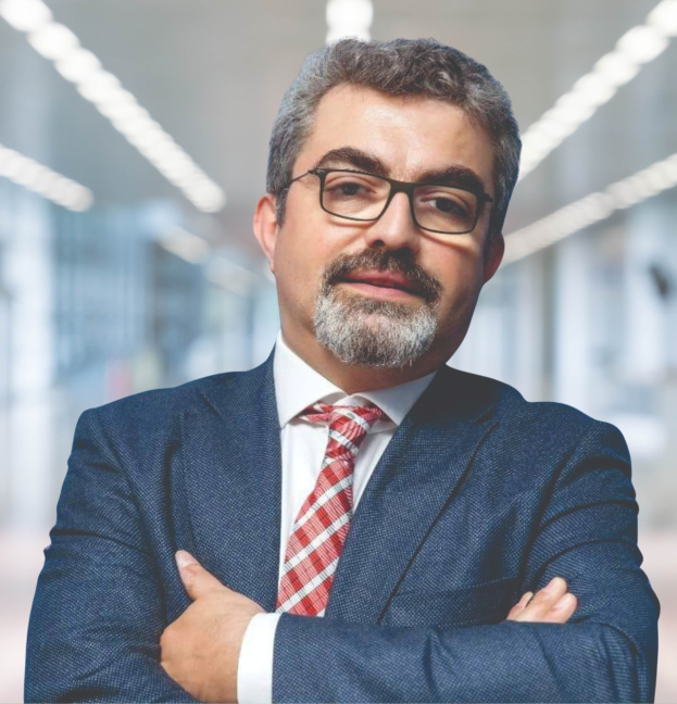 Ein Mann im Anzug mit verschränkten Armen und Brille steht vor einem unscharfen Hintergrund, als neuer Marketingchef bezeichnet.