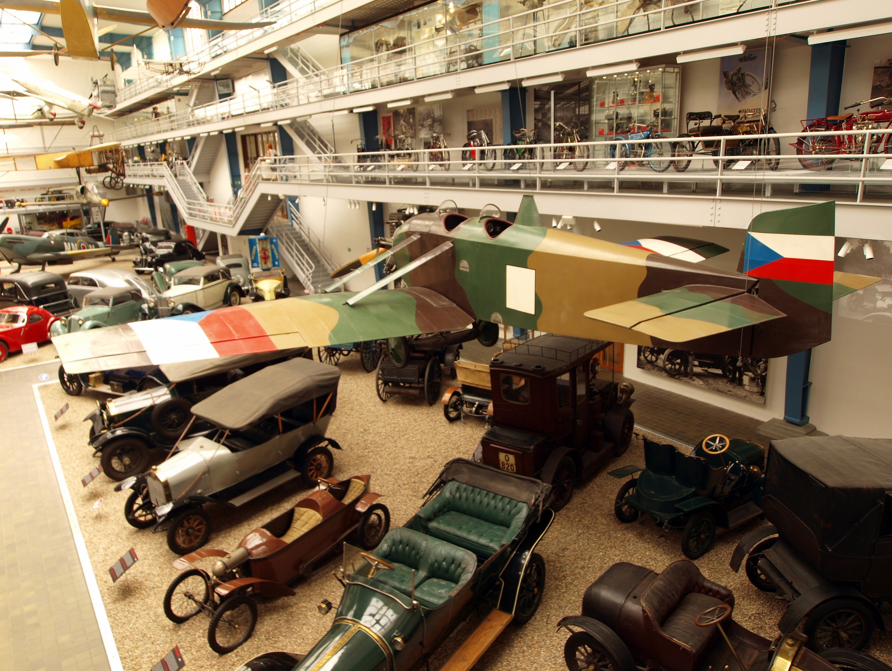 Ein großer Museumsraum mit Oldtimern, Flugzeugen, Fahrrädern und Informationsschildern, mit Besuchern, die die Ausstellungen betrachten.