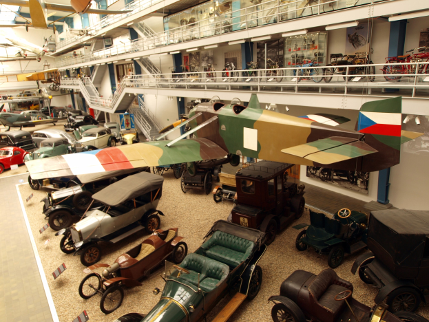 Ein großer Museumsraum mit Oldtimern, Flugzeugen, Fahrrädern und Informationsschildern, mit Besuchern, die die Ausstellungen betrachten.