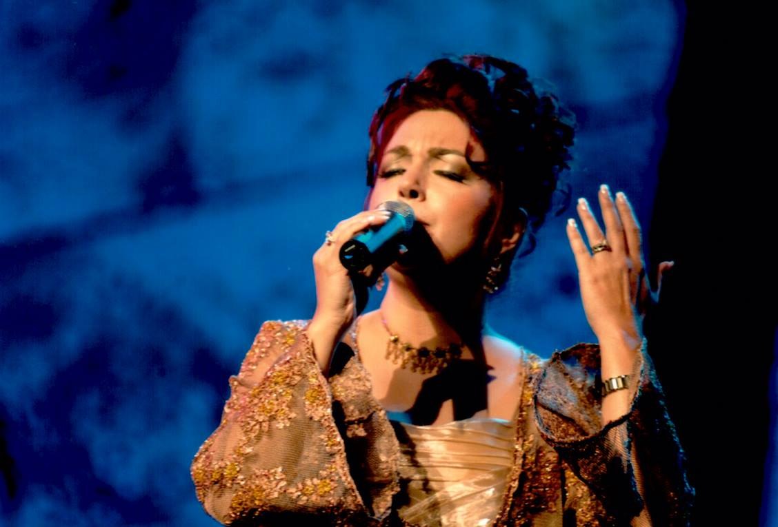 Frau in goldenem Kleid, die auf der Bühne der Eurovision Song Contest in ein Mikrofon singt.