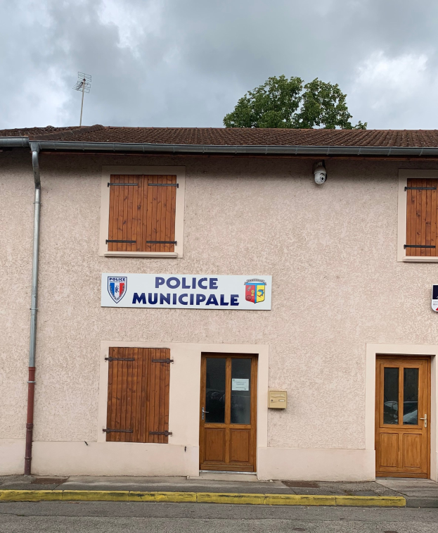 Polizeigebäude mit einem Schild, Fenstern, Türen, einem Namensschild, einem Rohr, einem Baum und einem bewölkten Himmel im Hintergrund.