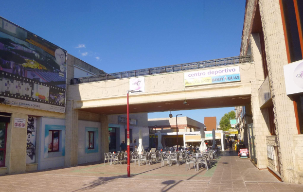 Ein belebter Stadtplatz mit Außensitzgelegenheiten, Straßeneinrichtungsgegenständen, Bäumen und einer bewölkten Himmel