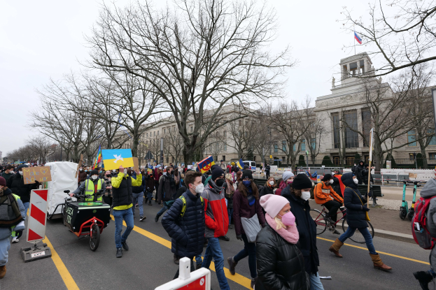 Eine große Gruppe von Menschen marschiert auf einer Stadtstraße in einem Protest, einige halten Schilder und andere fahren Fahrräder, mit Bäumen und einem Gebäude im Hintergrund unter einem klaren blauen Himmel in Washington, D.C. am 21. Januar 2020.