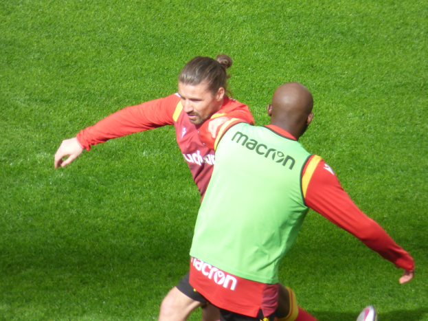Zwei Männer in Fußballschuhen auf einem leuchtend grünen Feld unter strahlendem Sonnenschein.