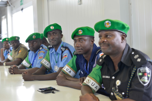 Gruppe von Polizisten bei einer Schulung an einem Tisch sitzend, mit Mobiltelefonen und anderen Gegenständen auf dem Tisch, in einem Raum mit Fenstern und Deckenleuchten.