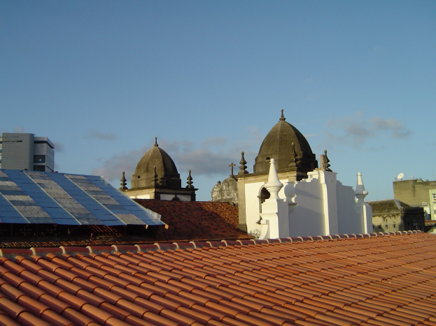 Stadtansicht mit einigen Gebäuden im Vordergrund und einem blauen Himmel im Hintergrund, mit Solarpanelen auf dem Dach eines Gebäudes.