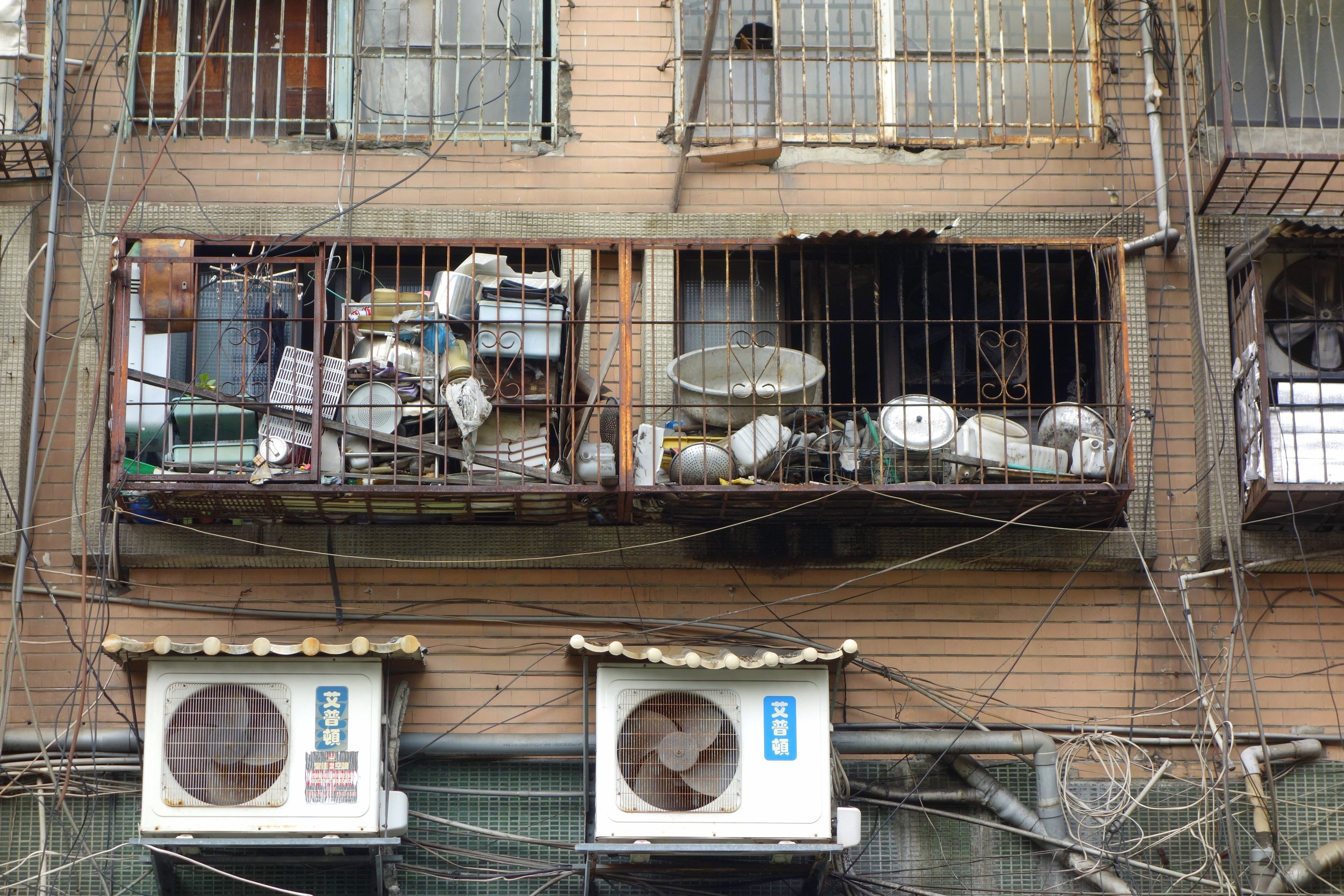 Wohngebäude mit Fenstern, Eisengittern, Klimaanlagen, Rohren und Kabeln an der Außenseite.